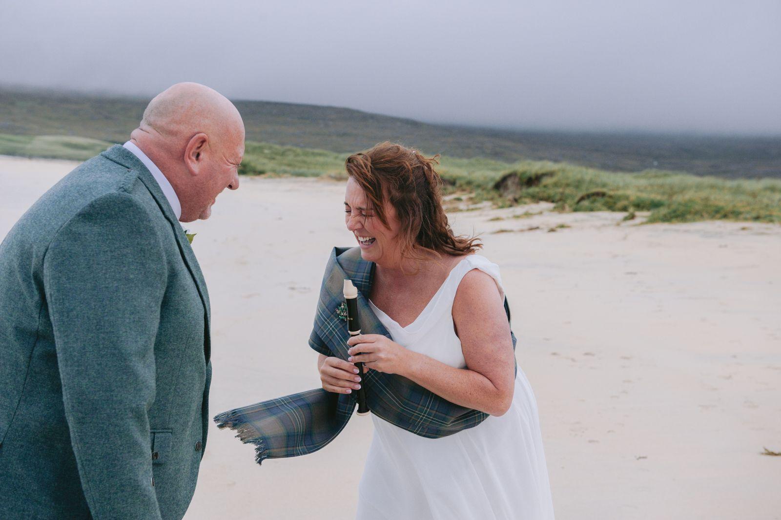 Bride laughing as she holds a tartan sash during her Seilebost beach wedding ceremony