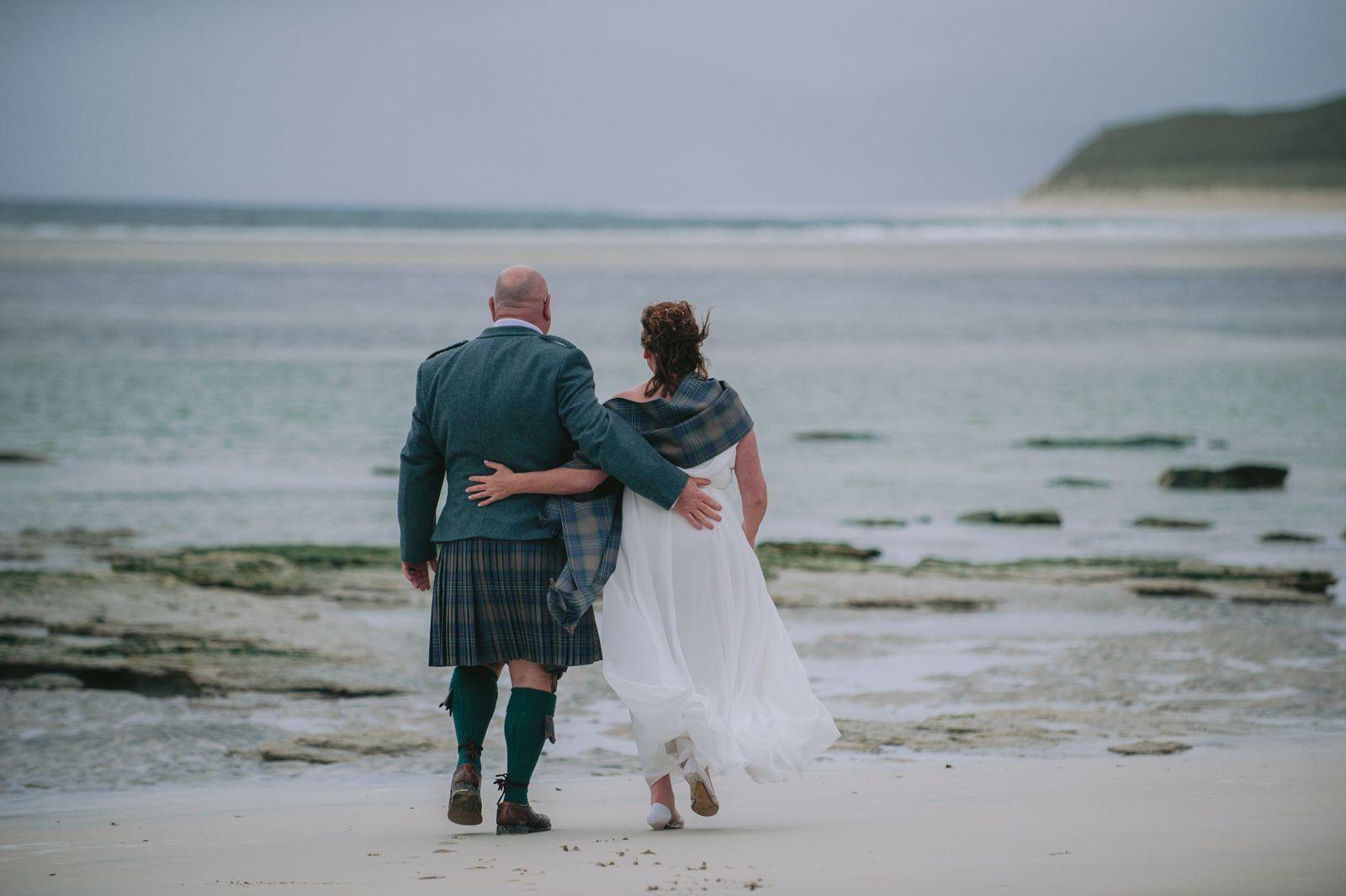 Bride and groom walking arm in arm along the shoreline at Seilebost on the Isle of Harris