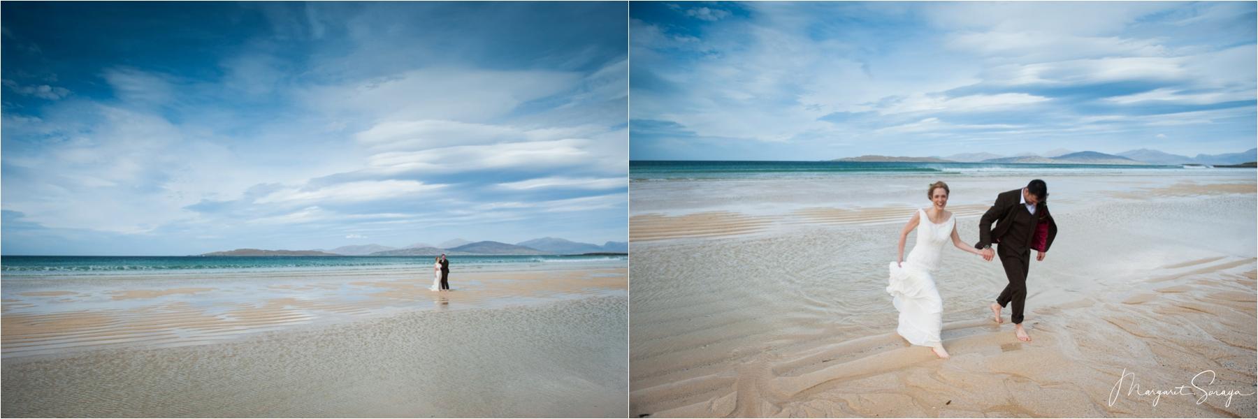 The bride and groom run barefoot up Scarista Beach under blue skies after their elopement in the Scottish Highlands. 