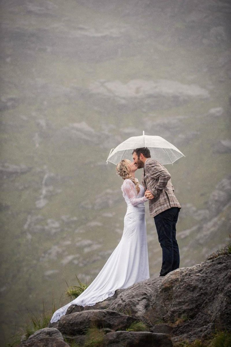A bride and groom stand on a mountain on the Isle of Skye under a white umbrella after their civil wedding ceremony.