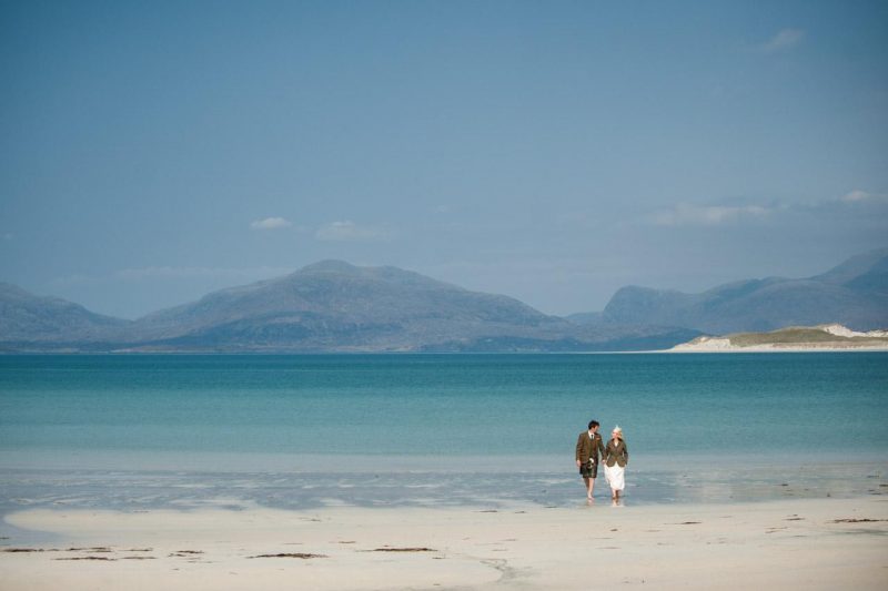 A bride and groom stand on the water's edge at Scarista Beach on the Isle of Harris.
