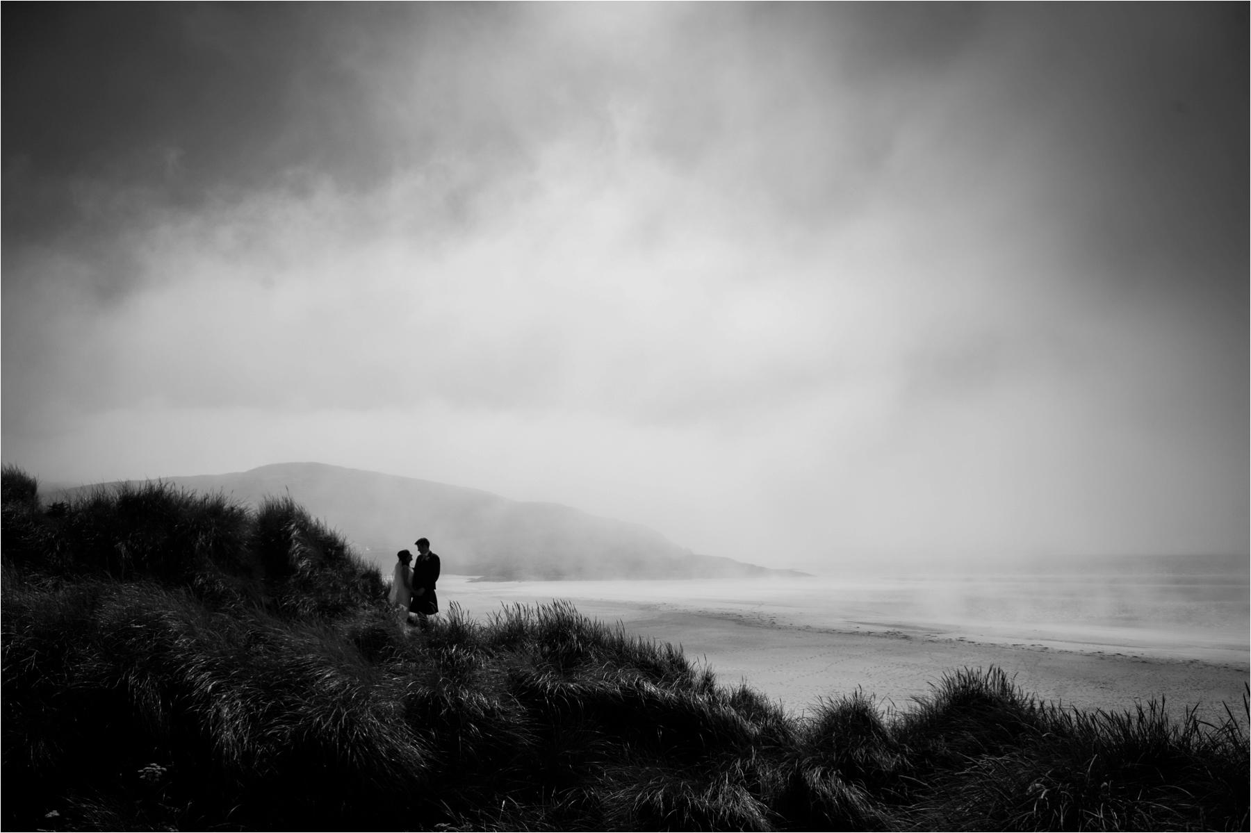 Black and white photo of a bride and groom with dramatic, storm skies near Luskentyre Beach in the Outer Hebrides. 