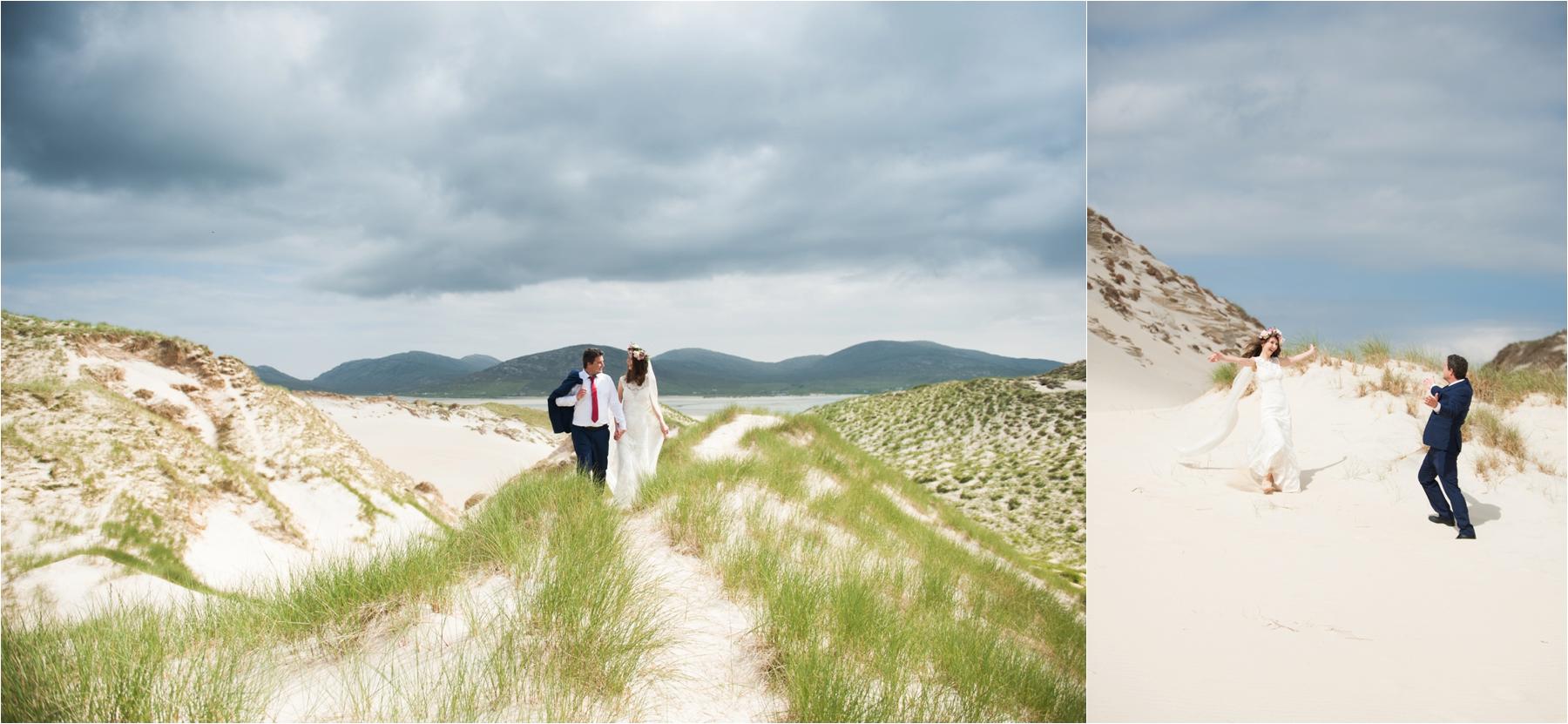 Bride and groom Ilona and Emil walk arm in arm and Emil has his jacket over his shoulder as they walk through sand dunes and sea grass on Luskentyre Beach. They married outdoors in front of two witnesses.