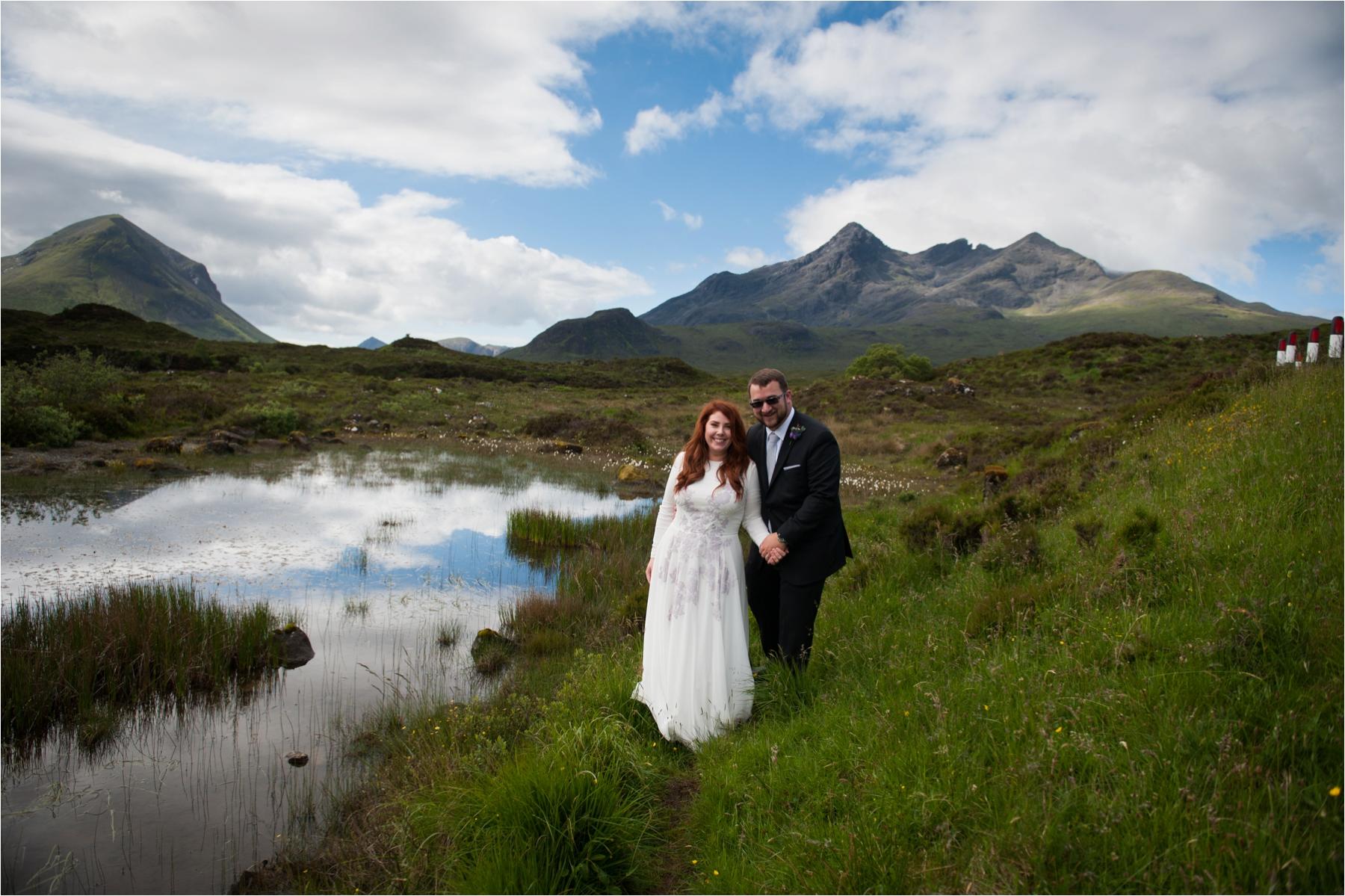 A bride and groom from Texas stand near water on the Isle of Skye after their outdoor wedding ceremony. 