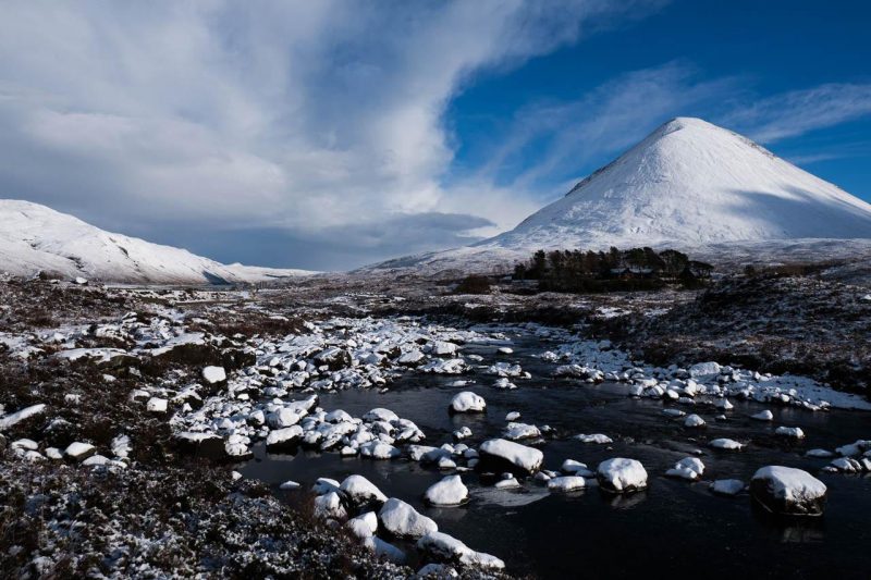 Snow covers mountains and rocks in an icy stream on the Isle of Skye in Scotland.