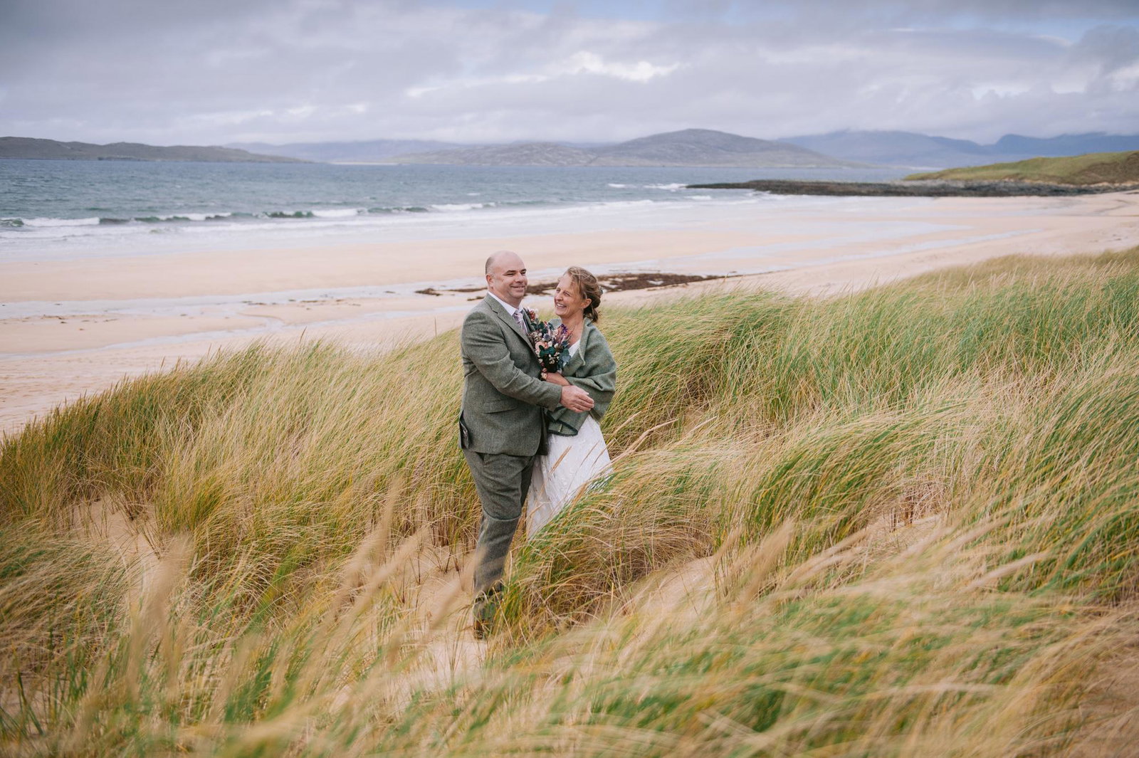 Bride and groom standing on Scarista Beach with the Harris hills behind them