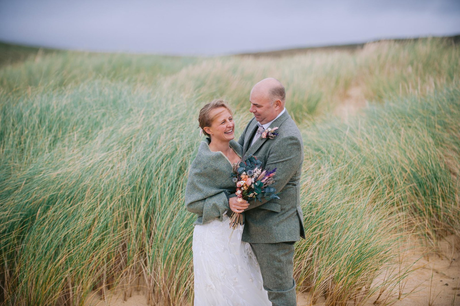 Bride and groom embracing among the dune grass above Scarista Beach