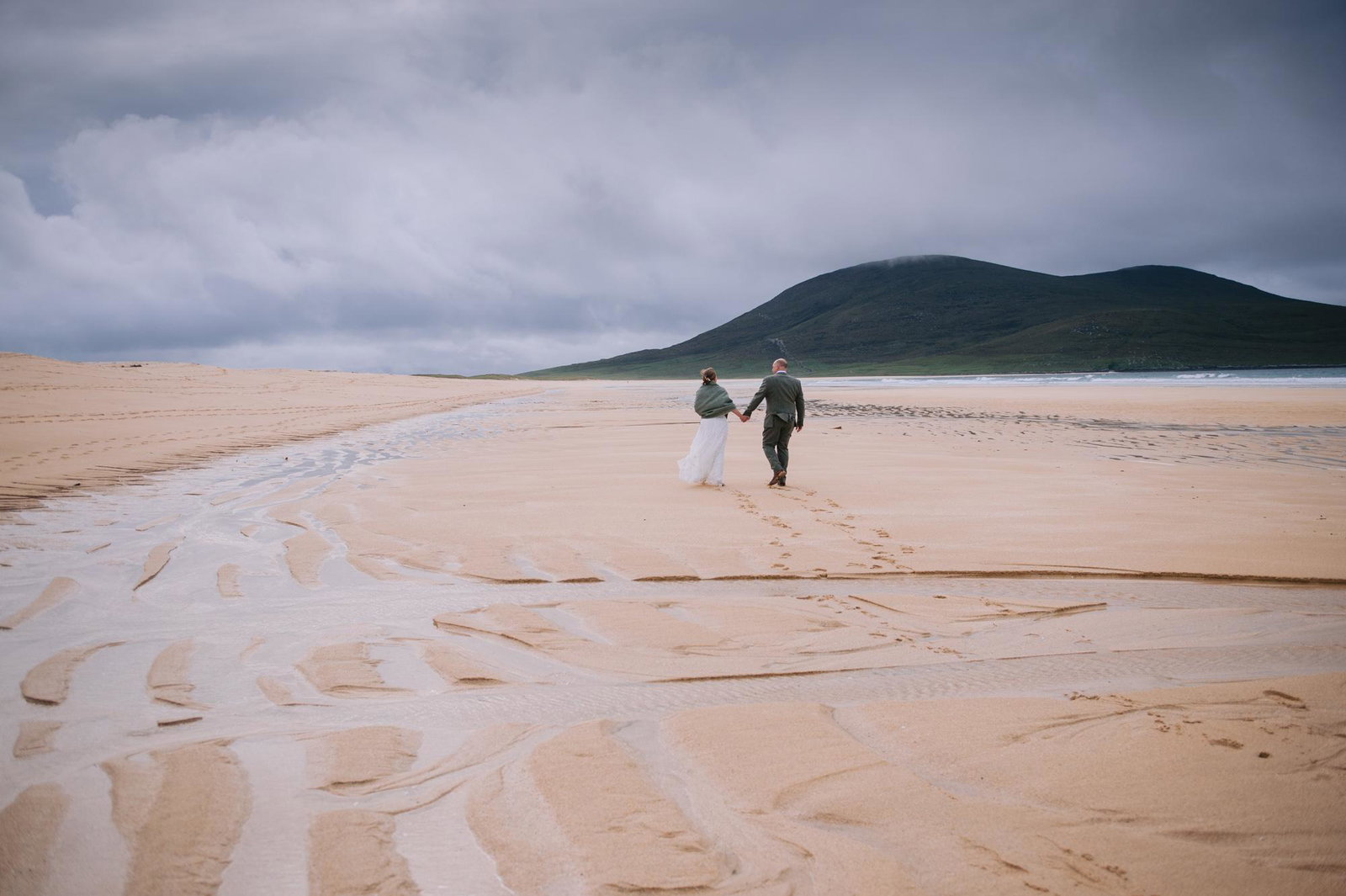 Couple walking hand in hand across the empty sand during their Scarista Beach elopement