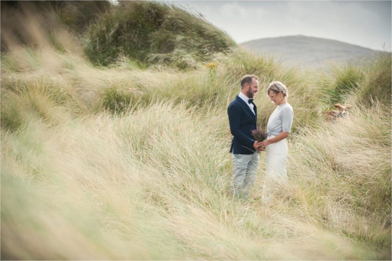 A bride and groom stand in the sand dunes on the Isle of Harris after their civil wedding ceremony.