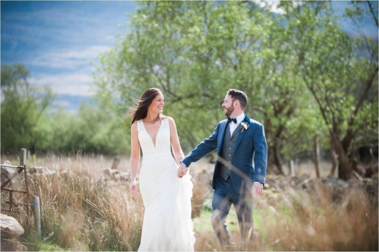 A bride and groom walk through a grassy field after their Scottish Highland wedding.