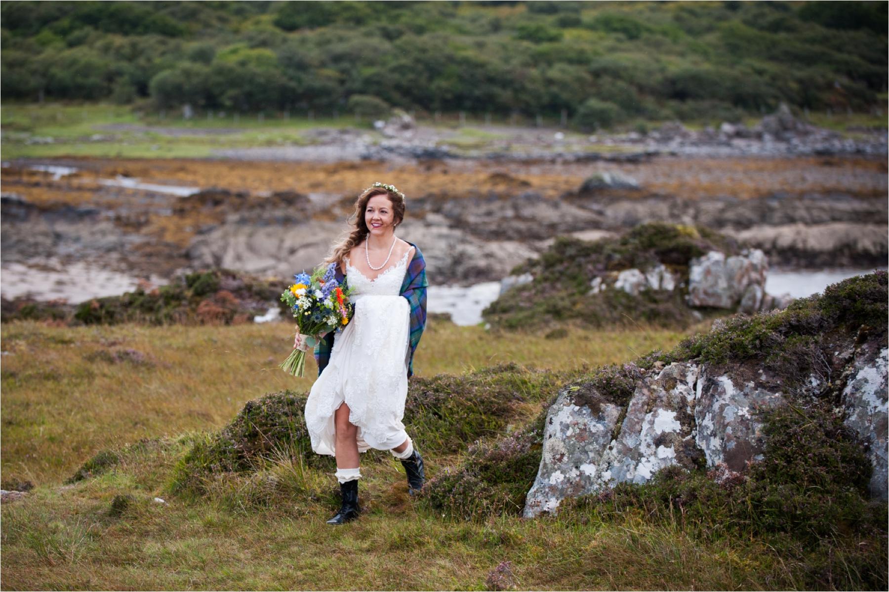 A bride dressed in a white wedding dress and black walking boots carries a colourful bouquet as she walks to her marriage ceremony in the ruined Dunscaith Castle. 