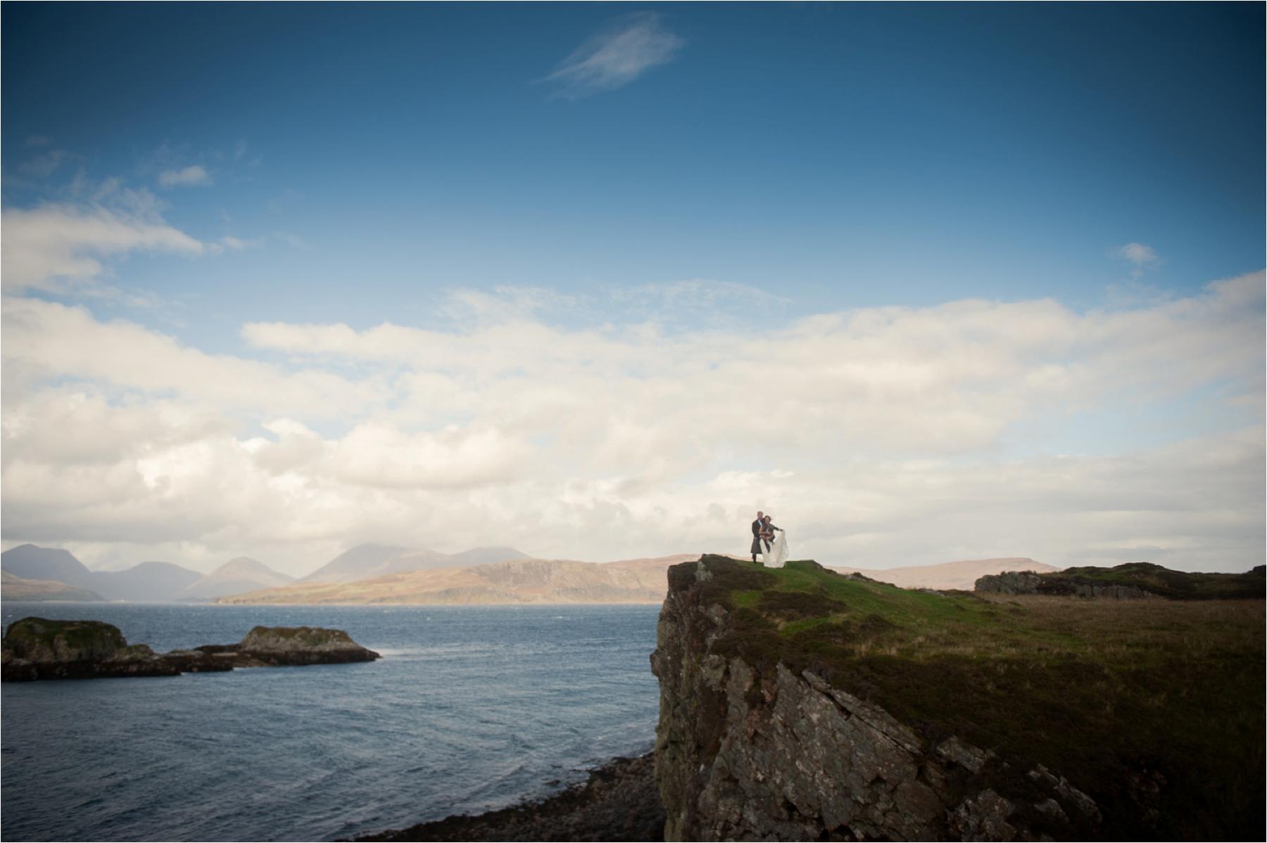 A bride and groom stand on a rocky cliff after their humanist wedding at Dunscaith Castle. Photographer: Margaret Soraya 