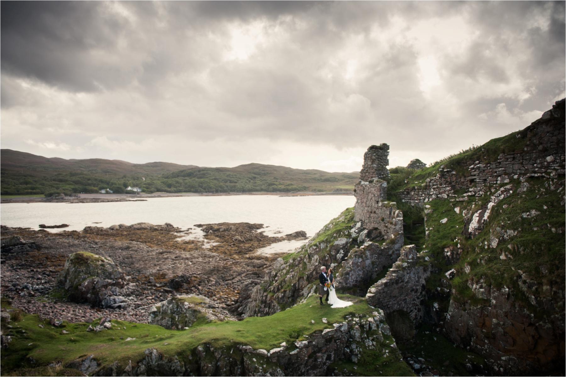 A couple exchange vows at Dunscaith Castle with the sun peeping through dramatic clouds. 